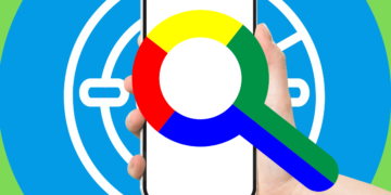Google could launch Find My Device network in early April. A hand holding a smartphone with the Google logo magnifying glass icon overlaid on a background of concentric circles in Google's colors.