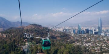 A cable car ascending a wire, the Santiago skyline and hills in the background.